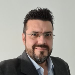Headshot photo of a man wearing glasses in a dark jacket